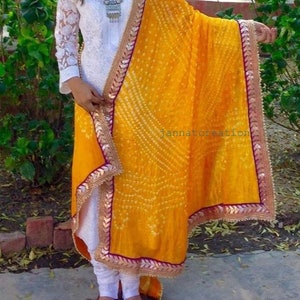 May include: A woman's white embroidered tunic and leggings paired with a vibrant yellow dupatta. The dupatta features a detailed pattern and a decorative border. The text "jannatcreation" is visible on the dupatta.