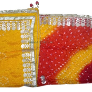 May include: A vibrant, colorful textile with a yellow and red gradient design. The fabric is adorned with small white dots and silver floral trim. The textile has a decorative tassel and a small floral embellishment.