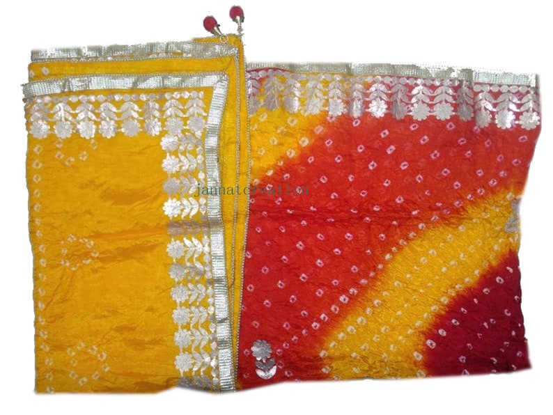 May include: A vibrant, colorful textile with a yellow and red gradient design. The fabric is adorned with small white dots and silver floral trim. The textile has a decorative tassel and a small floral embellishment.