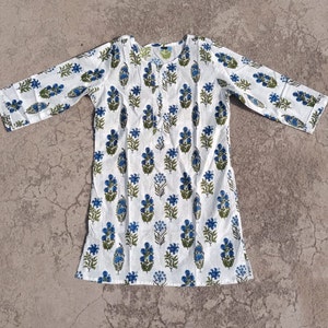 Puede incluir: Una t&uacute;nica de algod&oacute;n blanco con estampado floral azul y verde. La t&uacute;nica tiene mangas tres cuartos y un escote redondo.