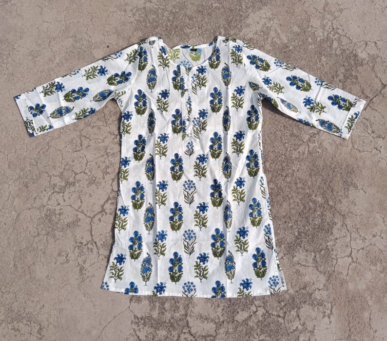 Puede incluir: Una t&uacute;nica de algod&oacute;n blanco con estampado floral azul y verde. La t&uacute;nica tiene mangas tres cuartos y un escote redondo.