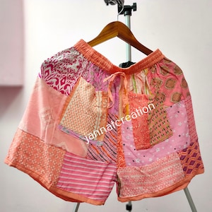 May include: Patchwork shorts in shades of pink, peach, and coral, with a drawstring waist. The shorts feature a variety of patterned fabric patches, including floral, geometric, and abstract designs. The text "jannatcreation" is visible on the shorts.