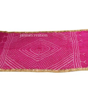 May include: A vibrant pink scarf with a geometric white pattern and a gold-colored border. The scarf has a rectangular shape and is likely made of a soft fabric. The text "jannatcreation" is visible on the scarf.