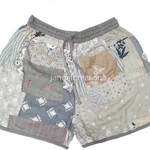 Peut inclure: Shorts patchwork aux tons de gris, beige et bleu, avec divers motifs floraux et géométriques. Le short a une taille élastique avec un cordon de serrage et est fait d'un tissu doux et léger. Le texte "jannatcreation" est visible.