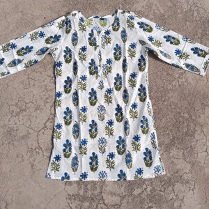 Puede incluir: T&uacute;nica de algod&oacute;n blanco con estampado floral azul y verde. La t&uacute;nica tiene un escote redondo y mangas tres cuartos.