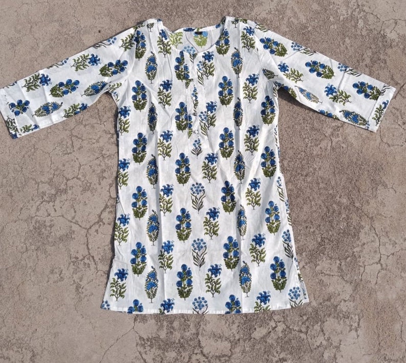 Puede incluir: T&uacute;nica de algod&oacute;n blanco con estampado floral azul y verde. La t&uacute;nica tiene un escote redondo y mangas tres cuartos.