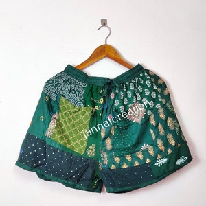 Puede incluir: Shorts verdes de patchwork con cintura de cordón. Los shorts están hechos de diferentes telas con varios patrones, incluyendo paisley, lunares y diseños florales. El texto "janmaicreator" es visible en los shorts.