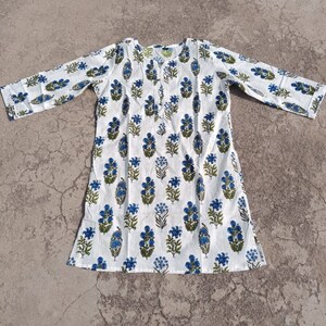 Puede incluir: T&uacute;nica de algod&oacute;n blanco con estampado floral azul y verde. La t&uacute;nica tiene mangas largas y un escote redondo.