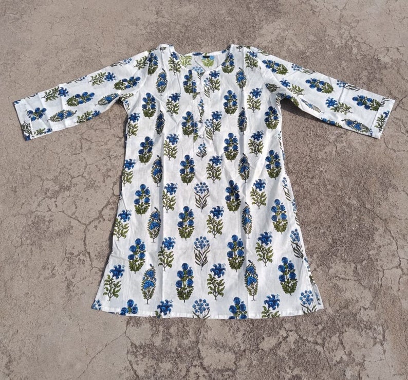 Puede incluir: T&uacute;nica de algod&oacute;n blanco con estampado floral azul y verde. La t&uacute;nica tiene mangas largas y un escote redondo.