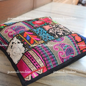 Puede incluir: Cojín cuadrado de patchwork con borde negro. El cojín presenta una variedad de parches de tela coloridos con diseños florales, paisley y geométricos. Los parches incluyen detalles en rosa, azul, verde y dorado.