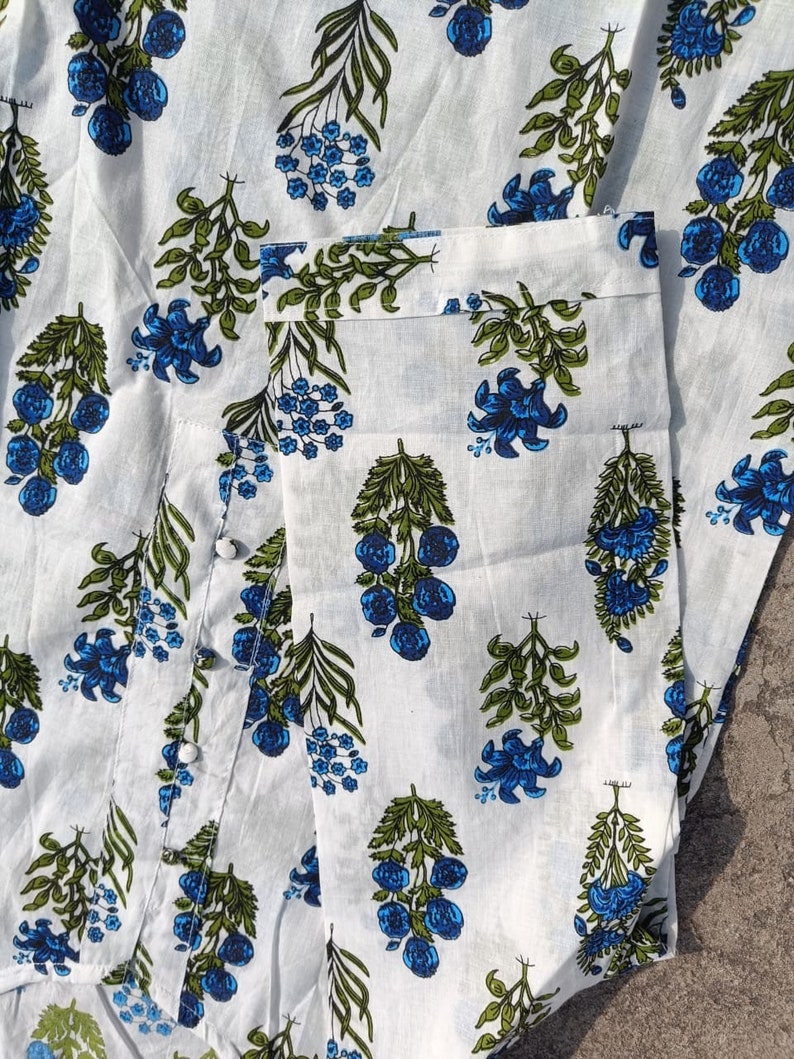 Puede incluir: Tela de algod&oacute;n blanca con estampado floral azul y verde. La tela tiene un brillo sutil y una textura suave.