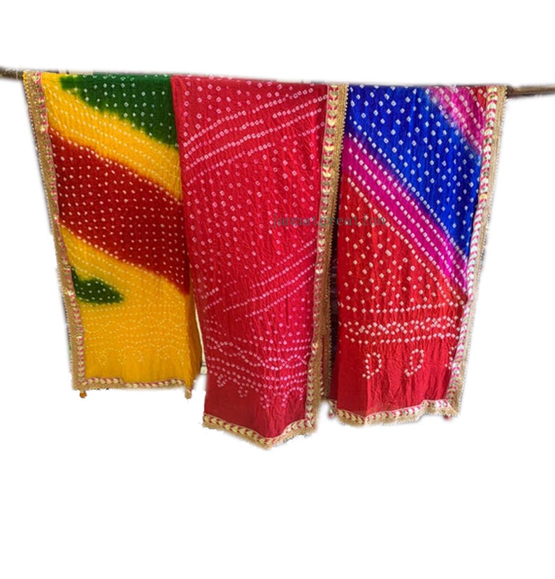 May include: Three colorful, patterned scarves hanging against a white background. The scarves are in shades of yellow, green, red, and blue, with white dot patterns and gold trim. The fabric appears to be lightweight.
