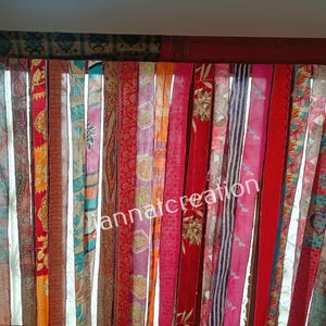 Peut inclure: Un rideau coloré composé de bandes de tissu verticales. Les bandes présentent divers motifs et couleurs, notamment du rouge, de l'orange, du bleu et des motifs floraux. Le haut et les côtés sont encadrés d'un tissu plus foncé, avec le texte "annatcreation".