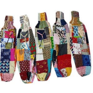 May include: Five bottle covers in a patchwork design, featuring a variety of colours and patterns. Each cover is constructed from different fabrics, including floral, geometric, and solid patterns. They have a drawstring closure at the top and are designed to fit around a bottle.