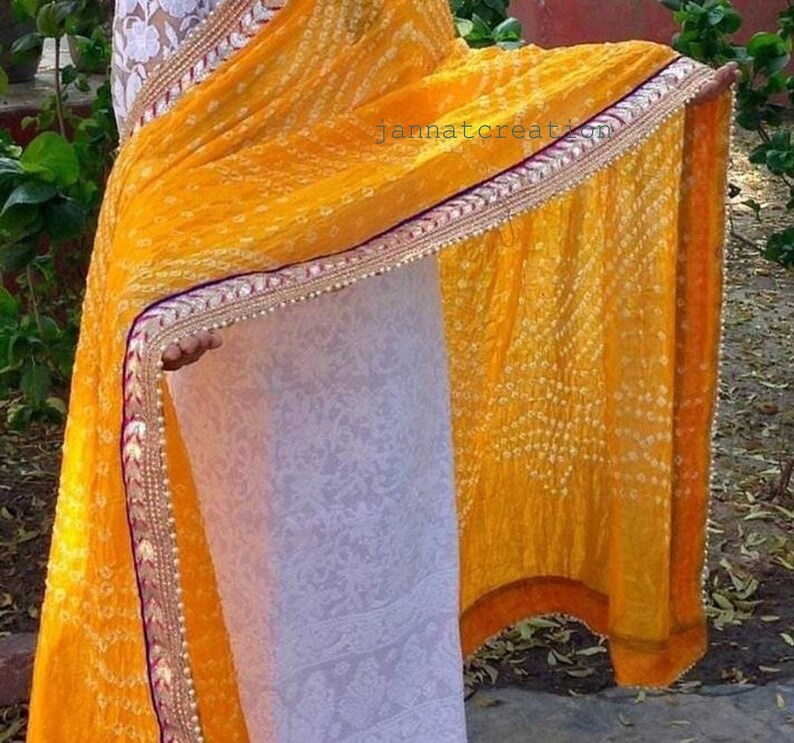 May include: A vibrant yellow saree with a detailed border. The saree features a dotted pattern and a decorative border with gold, red, and white accents. The text "jannatcreation" is visible on the fabric.