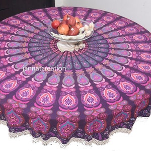 May include: A round purple tablecloth with a mandala design in shades of pink and teal. The tablecloth has a white lace trim and is topped with a glass bowl of red fruit. The text "jannatcreation" is visible.
