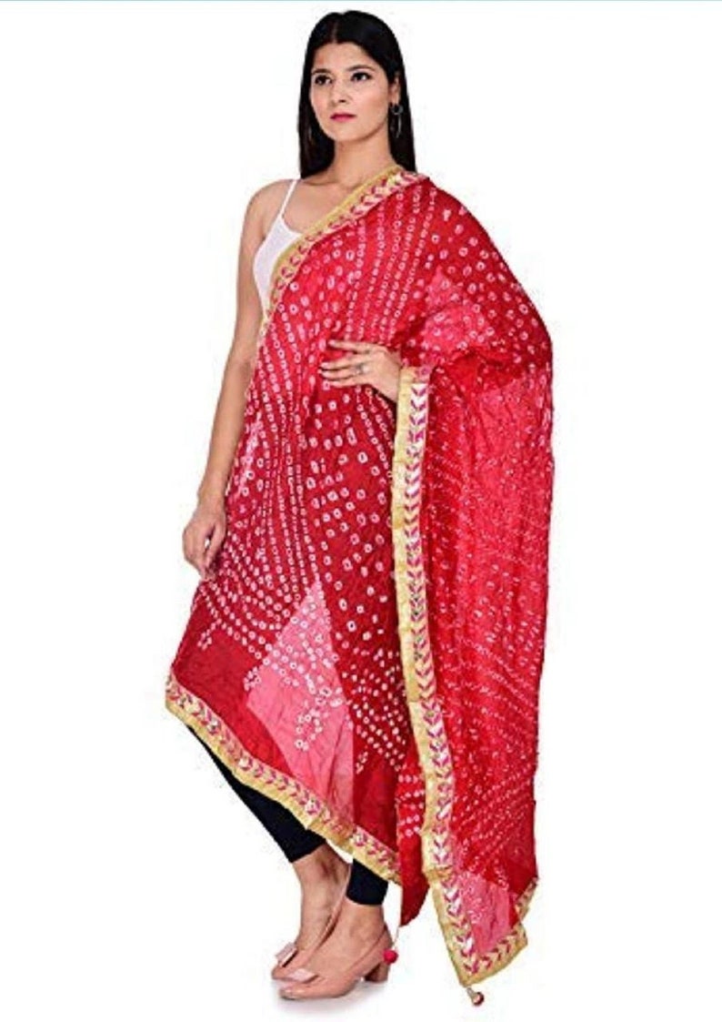May include: A vibrant red dupatta with a detailed white dot pattern and gold trim. The scarf is draped over the shoulder, showcasing its intricate design and flowing fabric. The dupatta adds a touch of elegance and color.