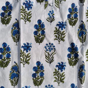 Puede incluir: Tela blanca con estampado floral azul y verde. La tela tiene un patr&oacute;n repetitivo de flores azules y hojas verdes.