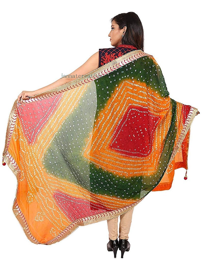 May include: A colorful, patterned scarf with a vibrant design. The scarf features a mix of orange, green, red, and pink hues, with a detailed border. The scarf is held open, showcasing its intricate patterns and textures.