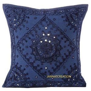 Puede incluir: Una funda de coj&iacute;n cuadrada de color azul marino con intrincados bordados en azul oscuro en un patr&oacute;n central de diamante y c&iacute;rculo, acentuada con peque&ntilde;os espejos reflectantes. El texto JANNATCREATION est&aacute; impreso en amarillo.