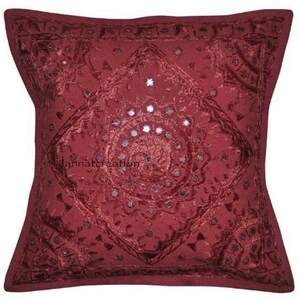 Puede incluir: Una funda de coj&iacute;n cuadrada de color rojo intenso con intrincados bordados tonales en un patr&oacute;n geom&eacute;trico de diamantes. El dise&ntilde;o est&aacute; adornado con peque&ntilde;os espejos circulares en el centro y los bordes. El texto jannatcreation es visible.