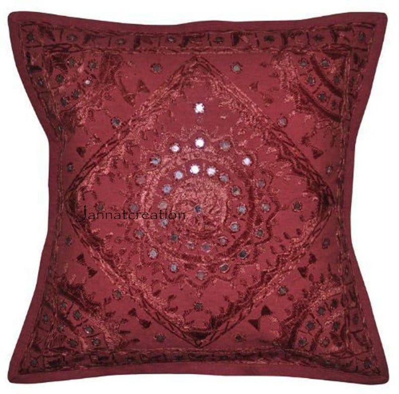 Puede incluir: Una funda de coj&iacute;n cuadrada de color rojo intenso con intrincados bordados tonales en un patr&oacute;n geom&eacute;trico de diamantes. El dise&ntilde;o est&aacute; adornado con peque&ntilde;os espejos circulares en el centro y los bordes. El texto jannatcreation es visible.