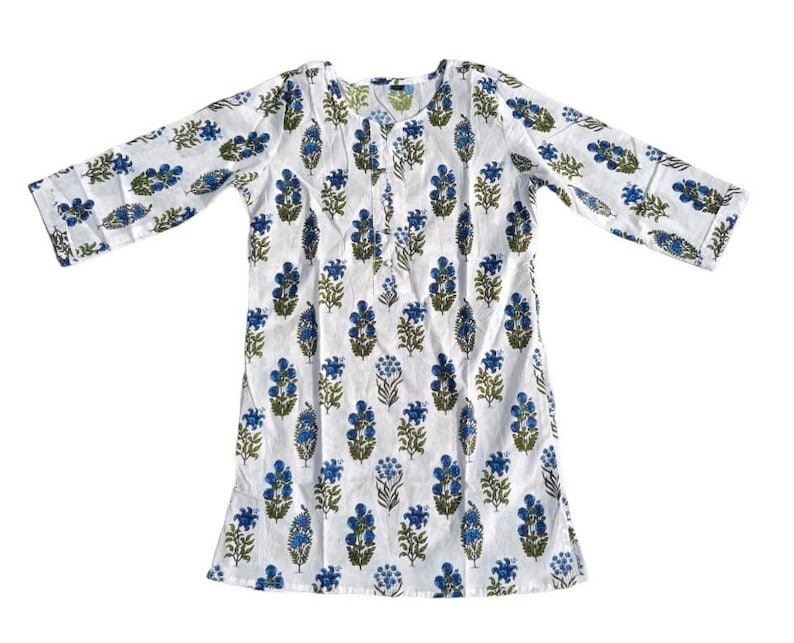 Puede incluir: T&uacute;nica de algod&oacute;n blanco con estampado floral azul y verde. La t&uacute;nica tiene un escote redondo y mangas tres cuartos.