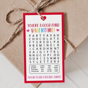 Op de afbeelding: Een rood en wit Valentijnsdag-cadeautje met een woordzoeker. De woordzoeker bevat de woorden "feest", "chocolade", "valentine", "liefde", "kus", "cadeau", "kaart" en meer. Het kaartje zegt "Je bent een goede vondst Valentine!" en "Van je vriend Jamie".