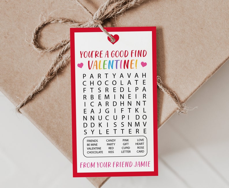 Op de afbeelding: Een rood en wit Valentijnsdag-cadeautje met een woordzoeker. De woordzoeker bevat de woorden "feest", "chocolade", "valentine", "liefde", "kus", "cadeau", "kaart" en meer. Het kaartje zegt "Je bent een goede vondst Valentine!" en "Van je vriend Jamie".
