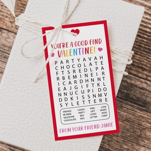 Op de afbeelding: Een rood-witte Valentijnskaart met een woordzoeker. De woordzoeker bevat woorden zoals "feest", "chocolade", "valentine", "liefde", "hart", "cadeau", "kus" en "cupido". De kaart zegt "Je bent een goede vondst Valentine!" en "Van je vriend Jamie".