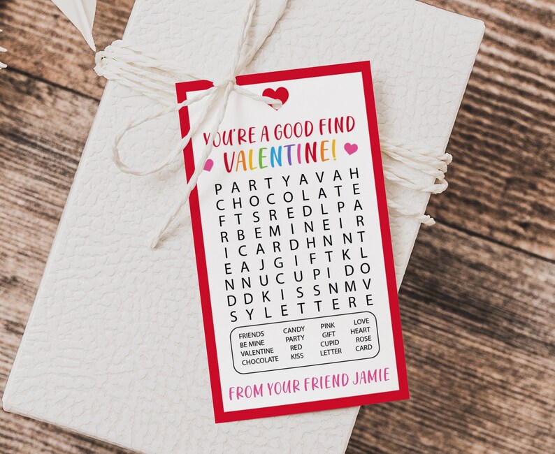 Op de afbeelding: Een rood-witte Valentijnskaart met een woordzoeker. De woordzoeker bevat woorden zoals "feest", "chocolade", "valentine", "liefde", "hart", "cadeau", "kus" en "cupido". De kaart zegt "Je bent een goede vondst Valentine!" en "Van je vriend Jamie".