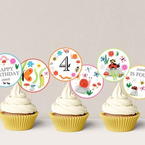 Puede incluir: Cuatro adornos para cupcakes con temática de insectos. Los adornos presentan una mariposa, un caracol, una mariquita y un número cuatro. El texto en los adornos dice "Feliz cumpleaños Jamie" y "Jamie tiene cuatro años".