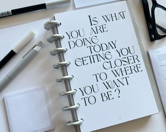 May include: A white planner with a motivational quote: "Is what you are doing today setting you closer to where you want to be?"
