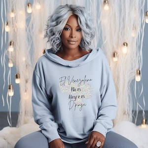 May include: A light blue hooded sweatshirt with the text "El Venezolano No es Alegre es Dpinga" printed on the front. The text is in black and is surrounded by a colorful, glittery design.