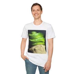 May include: White t-shirt with a print of a bright green snake coiled on a piece of wood. The snake's scales are detailed against a dark background. The t-shirt is a casual, everyday wear item, suitable for various occasions.