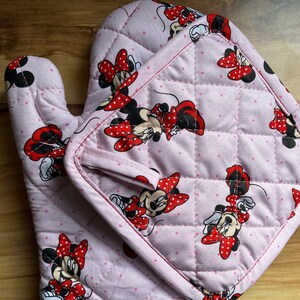May include: Pink quilted oven mitt and pot holder set with a Minnie Mouse print. The set features a red and white polka dot pattern and a Minnie Mouse design.