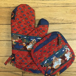 May include: A set of two red and blue quilted oven mitts with a Southwestern design featuring women in traditional clothing. The mitts are quilted with a diamond pattern and have a hanging loop.