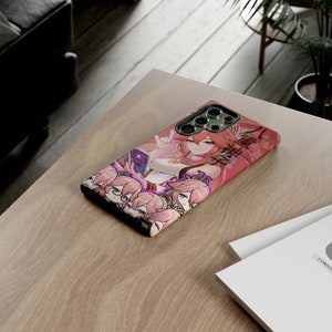 May include: A pink and red phone case with a colorful anime character design. The case features a female character with pink hair and a purple outfit. The case has a camera lens cutout and a raised lip around the edges.