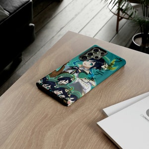 May include: A green and blue phone case with a cartoon character design. The character has blue hair and is wearing a green and white outfit. The case has a camera lens cutout and a raised edge around the screen.