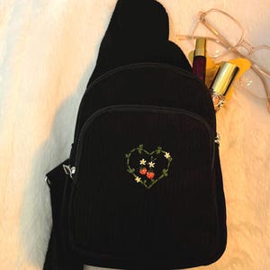 May include: Black corduroy crossbody bag with a small embroidered heart featuring strawberries and flowers.