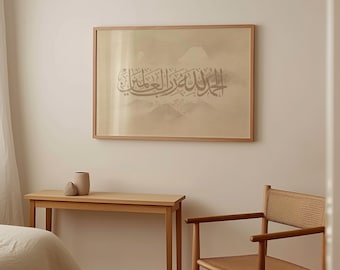 May include: A rectangular wall art piece in a light wood frame featuring Arabic calligraphy in dark grey ink on a beige background with a faint mountain landscape illustration behind the text, displayed on a plain wall.