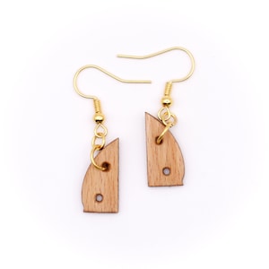 May include: A pair of gold earrings with wooden sailboat charms. The sailboats are light brown and have two holes in them.