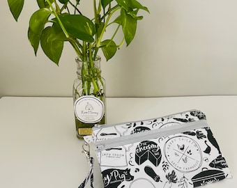 May include: A white zippered pouch with a black and white print of various food and farm-related illustrations. The print includes text such as "The Cheesy Pig", "Lazy Spoon", and "Happy Chicken Dream Farmhouse". The pouch has a black and white strap.