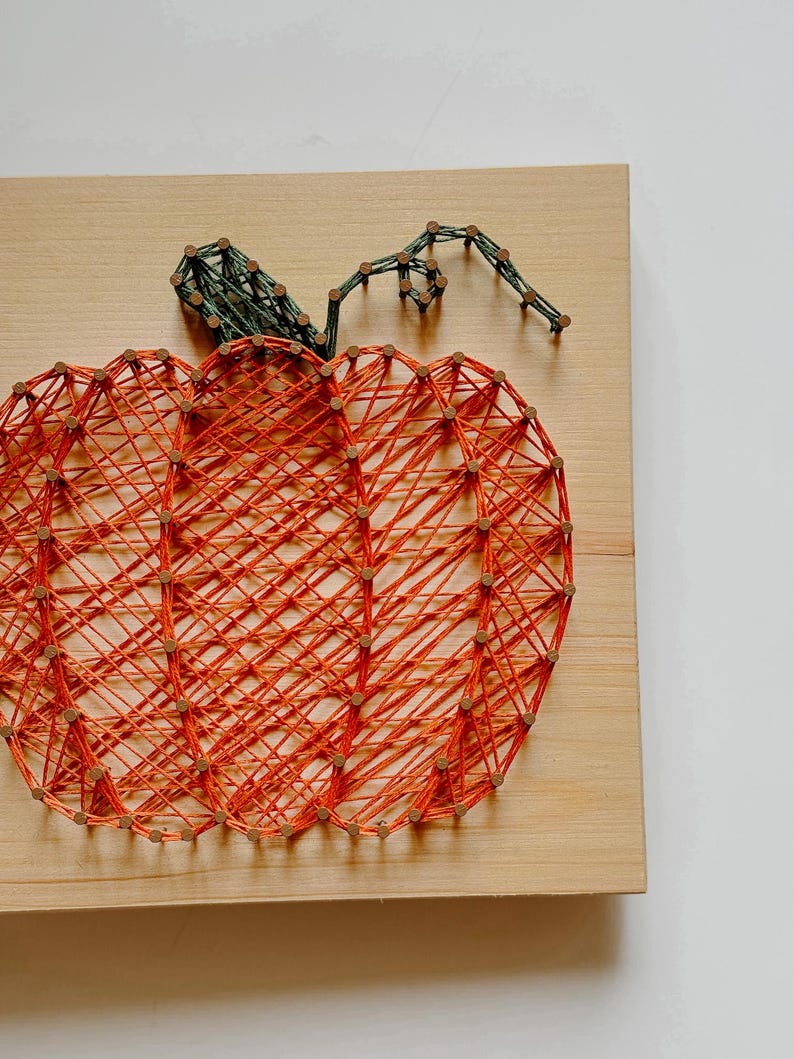 K&ouml;nnte beinhalten: Orangefarbener und gr&uuml;ner String-Art-K&uuml;rbis auf einem Holzgrund.