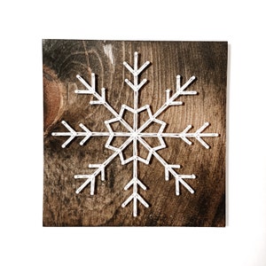 Peut inclure: Un flocon de neige en fil blanc sur un fond de bois brun fonc&eacute;.