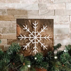 Peut inclure: Une flocon de neige en fil blanc sur un fond de bois brun fonc&eacute;. Le flocon de neige est un motif simple &agrave; six branches et un petit cercle au centre.