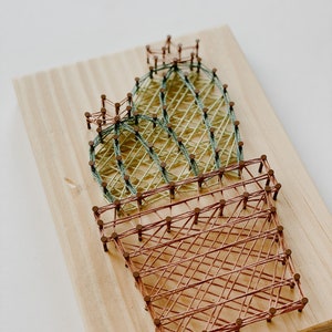 May include: A string art cactus with green and brown thread wrapped around nails hammered into a wooden board.
