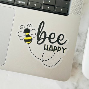 May include: A black and yellow bee sticker on a silver laptop with the text "bee happy".