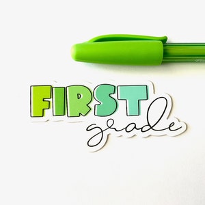 May include: A green, white, and blue sticker with the text "FIRST grade" in a colorful, playful font. The sticker is on a white background.