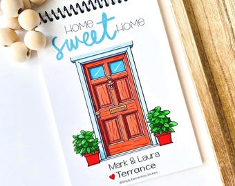 Może przedstawiać: Spiralny notatnik z kolorową ilustracją drzwi wejściowych. Słowa "Home Sweet Home" są napisane niebieskim pismem nad drzwiami. Drzwi są pomarańczowe z niebieskimi szybami i są otoczone dwoma doniczkowymi zielonymi roślinami. Poniżej drzwi widnieją imiona "Mark & Laura Terrance".